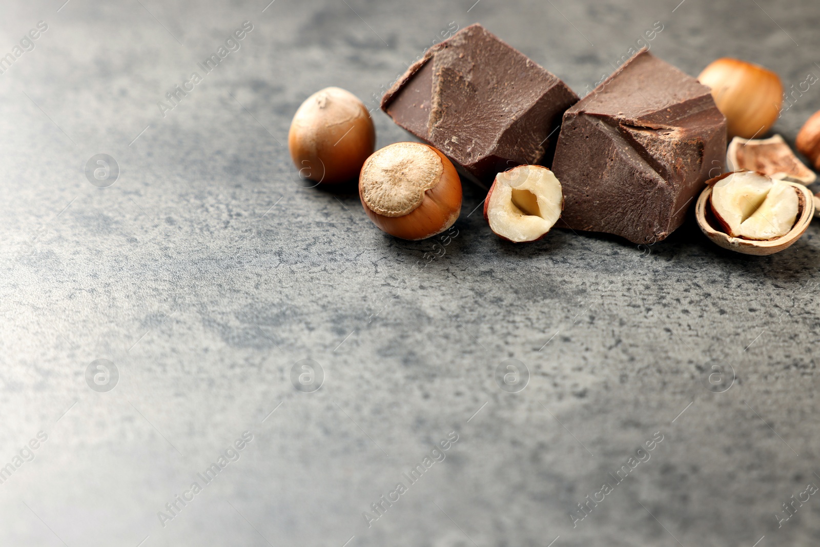 Photo of Delicious chocolate chunks and hazelnuts on grey table. Space for text