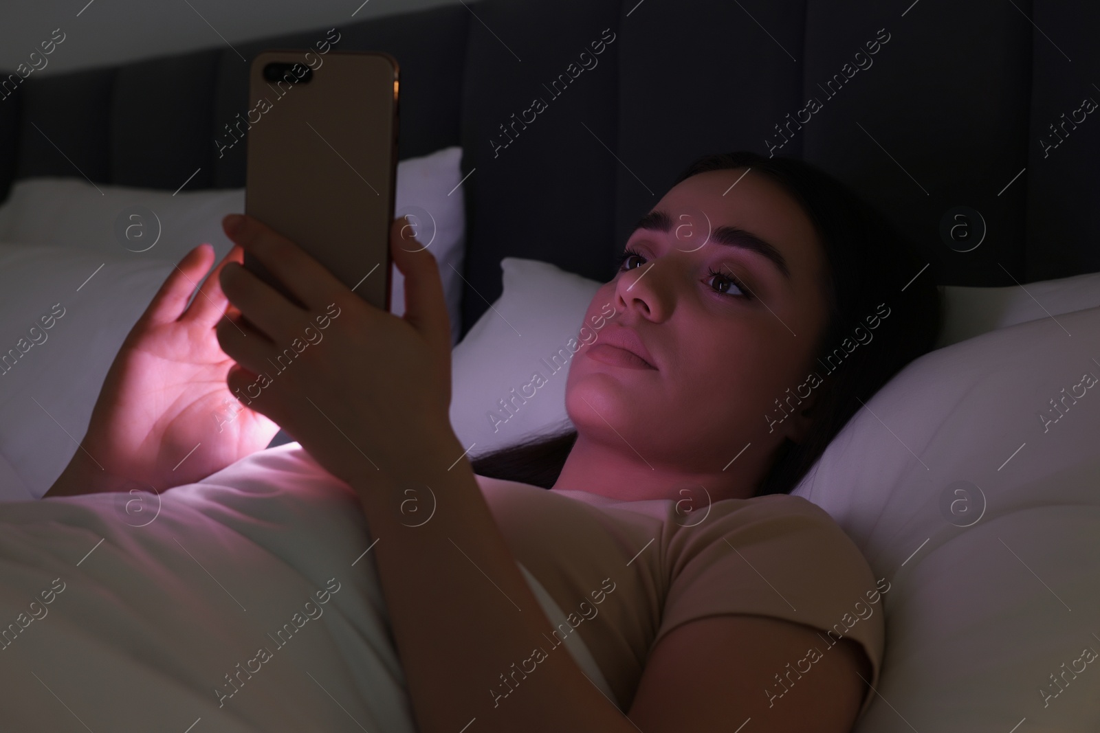Photo of Young woman using modern smartphone in bed at night. Internet addiction