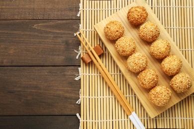 Delicious sesame balls and chopsticks on wooden table, top view. Space for text