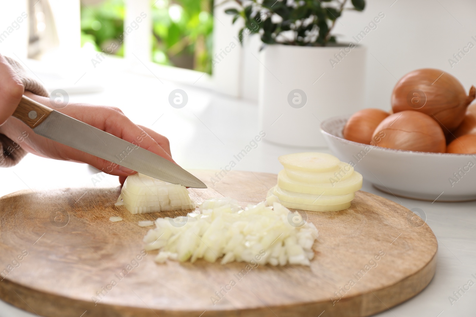 Photo of Woman chopping white onion on wooden board at table, closeup