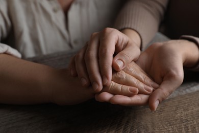 Woman holding hands with her mother at wooden table, closeup