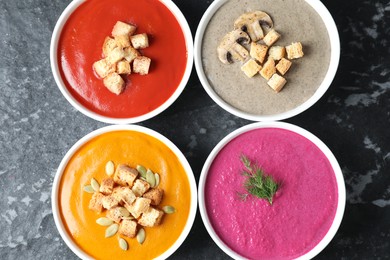 Different tasty cream soups in bowls on black textured table, flat lay