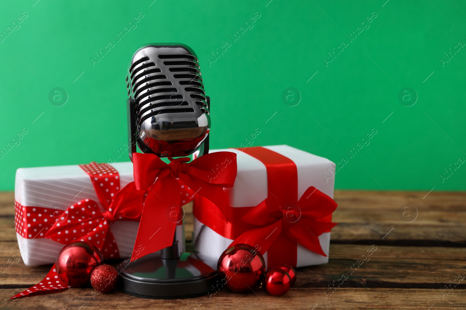 Photo of Retro microphone with red bow, gift boxes and festive decor on wooden table against green background, space for text. Christmas music