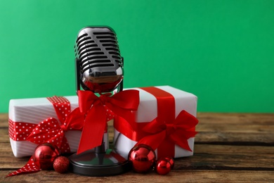 Retro microphone with red bow, gift boxes and festive decor on wooden table against green background, space for text. Christmas music