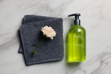 Dispenser of liquid soap, towel and rose on white marble table, flat lay