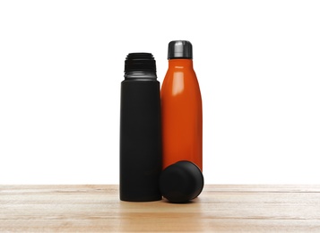 Stylish thermo bottles on wooden table against white background