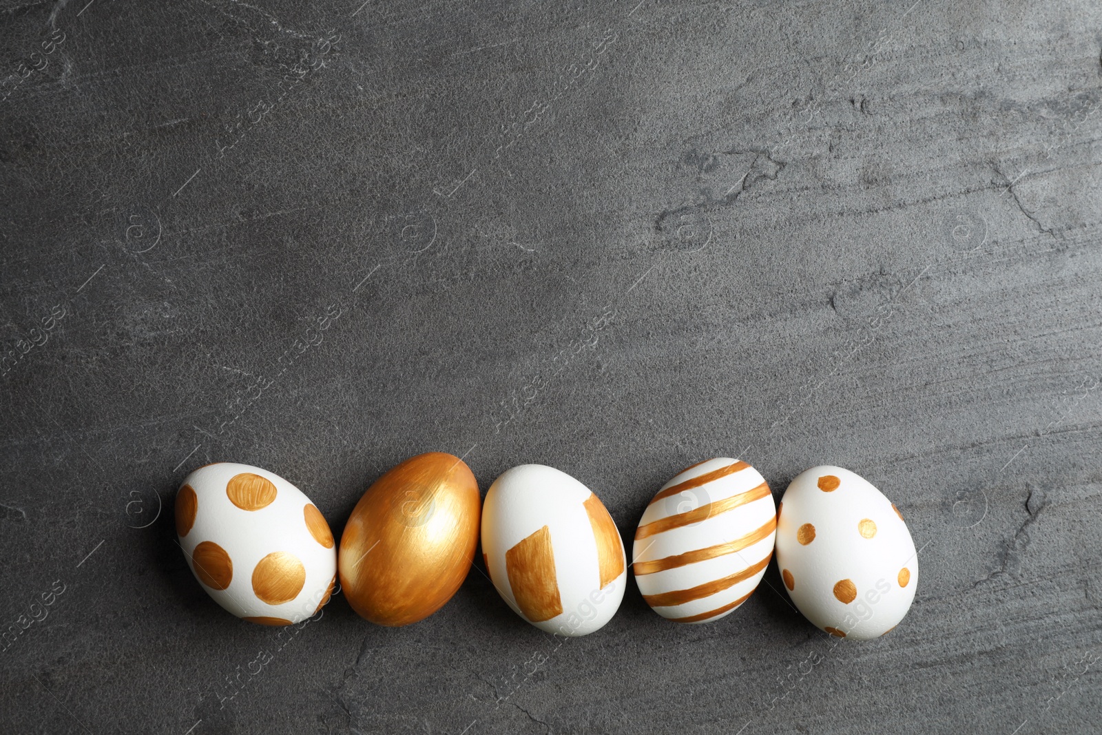 Photo of Set of traditional Easter eggs decorated with golden paint on grey background, top view. Space for text