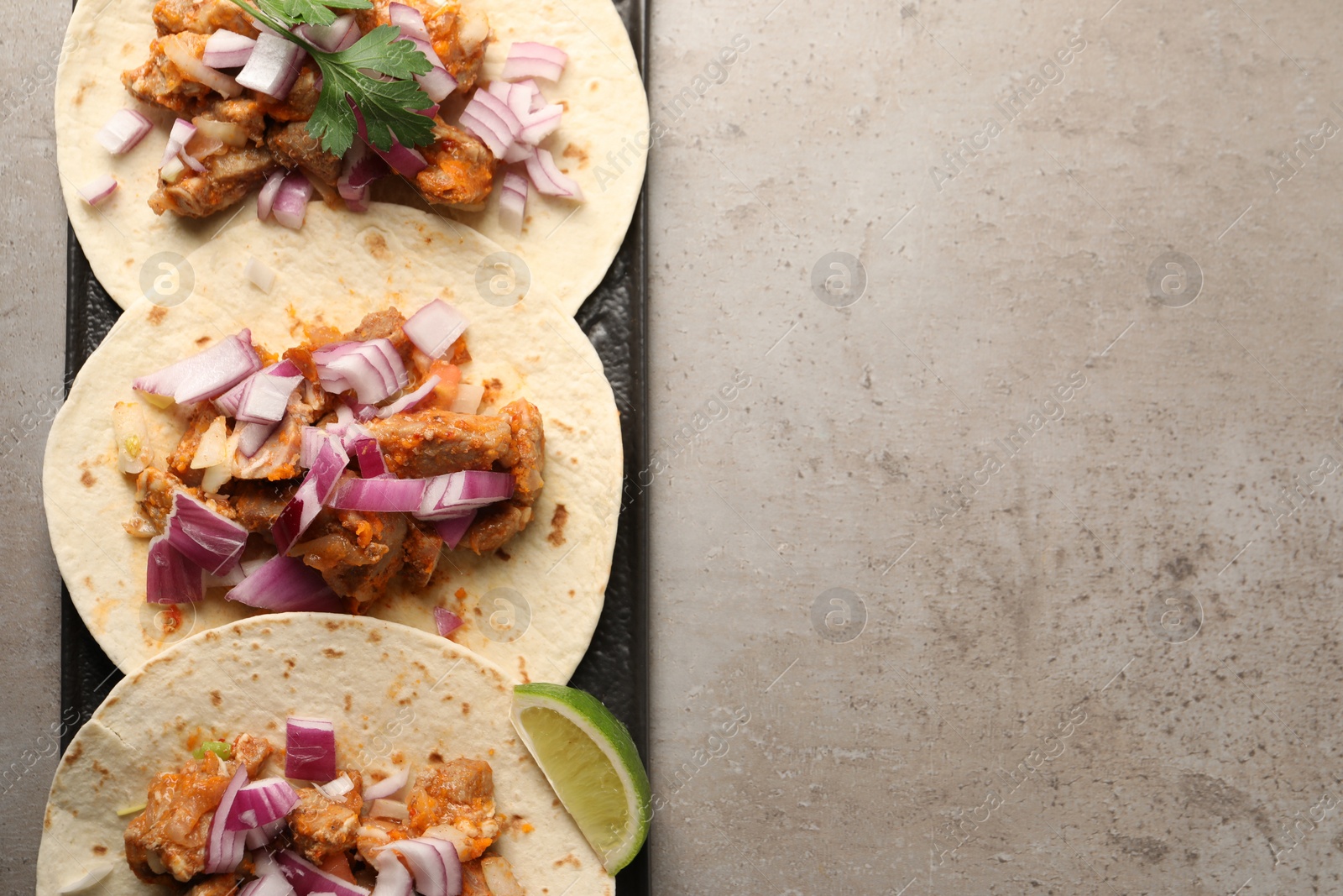 Photo of Delicious tacos with vegetables, meat and lime on grey textured table, top view. Space for text