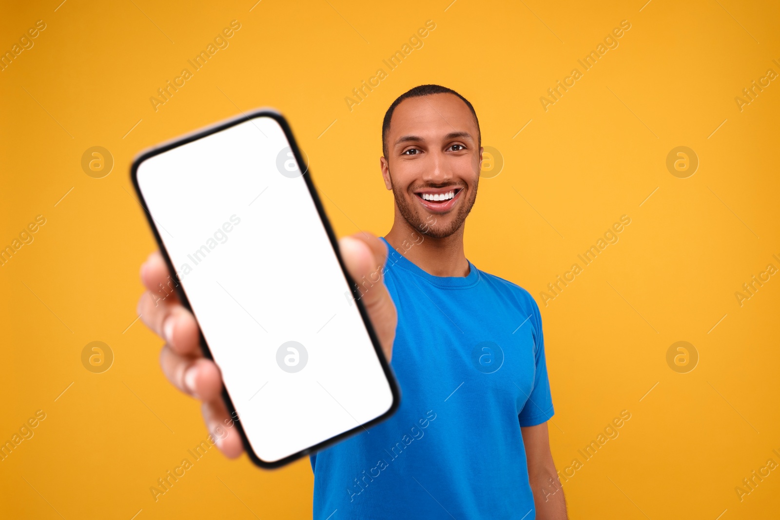 Photo of Young man showing smartphone in hand on yellow background