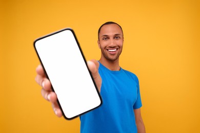 Young man showing smartphone in hand on yellow background
