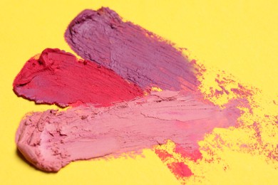 Smears of different beautiful lipsticks on yellow background, closeup