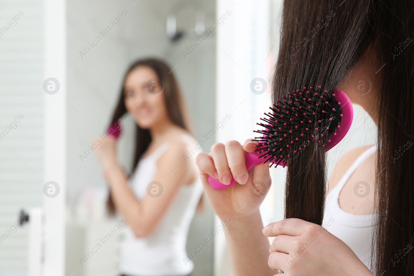 Photo of Beautiful young woman with hair brush looking into mirror in bathroom