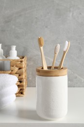 Photo of Bamboo toothbrushes in holder, towels and cosmetic products on white countertop
