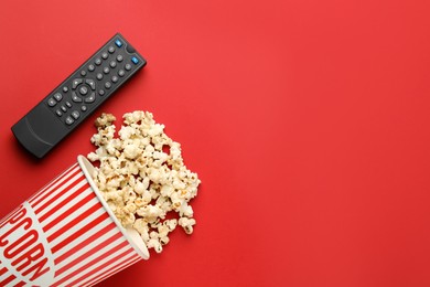 Remote control and cup of popcorn on red background, flat lay. Space for text