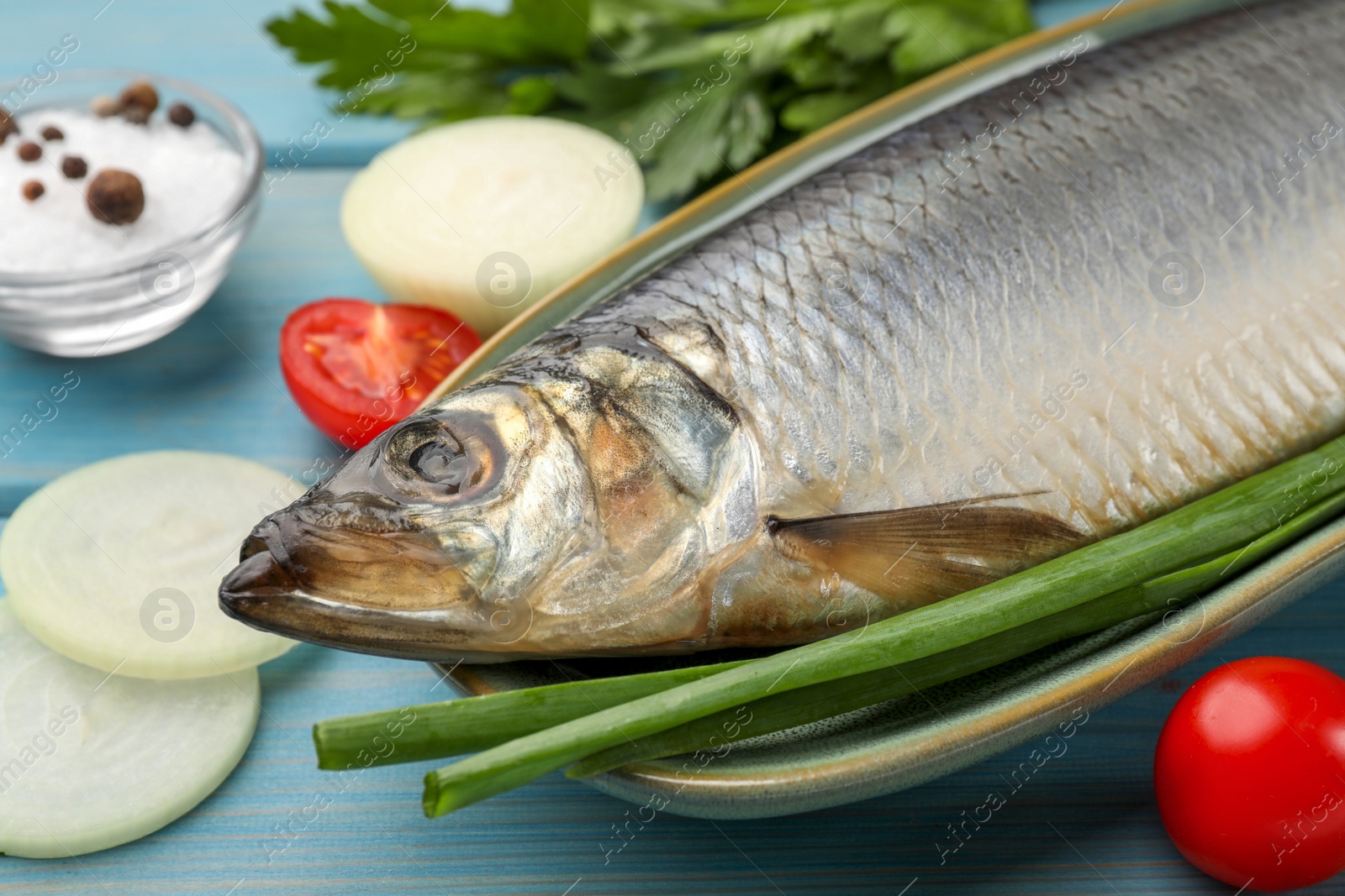 Photo of Delicious salted herring and ingredients on light blue wooden table, closeup