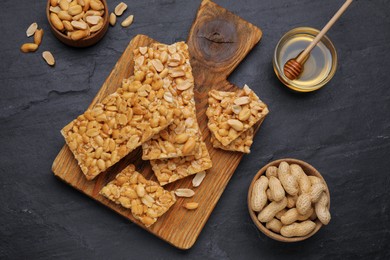 Photo of Delicious peanut bars (kozinaki) and ingredients on black table, flat lay