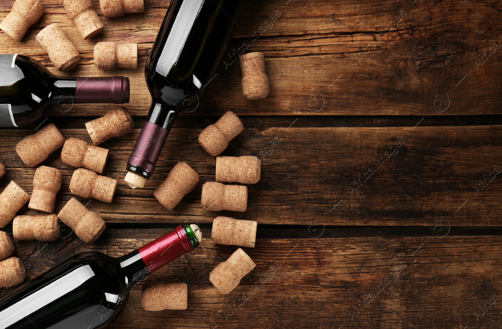 Photo of Bottles with wine, corkscrew and corks on wooden table, flat lay. Space for text