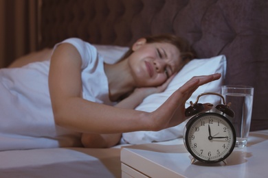 Photo of Young woman with terrible headache at night trying to turn off alarm clock