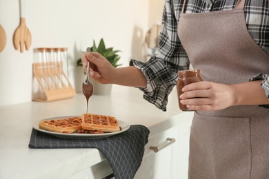 Photo of Woman decorating delicious Belgian waffles with chocolate cream at white countertop in kitchen, closeup