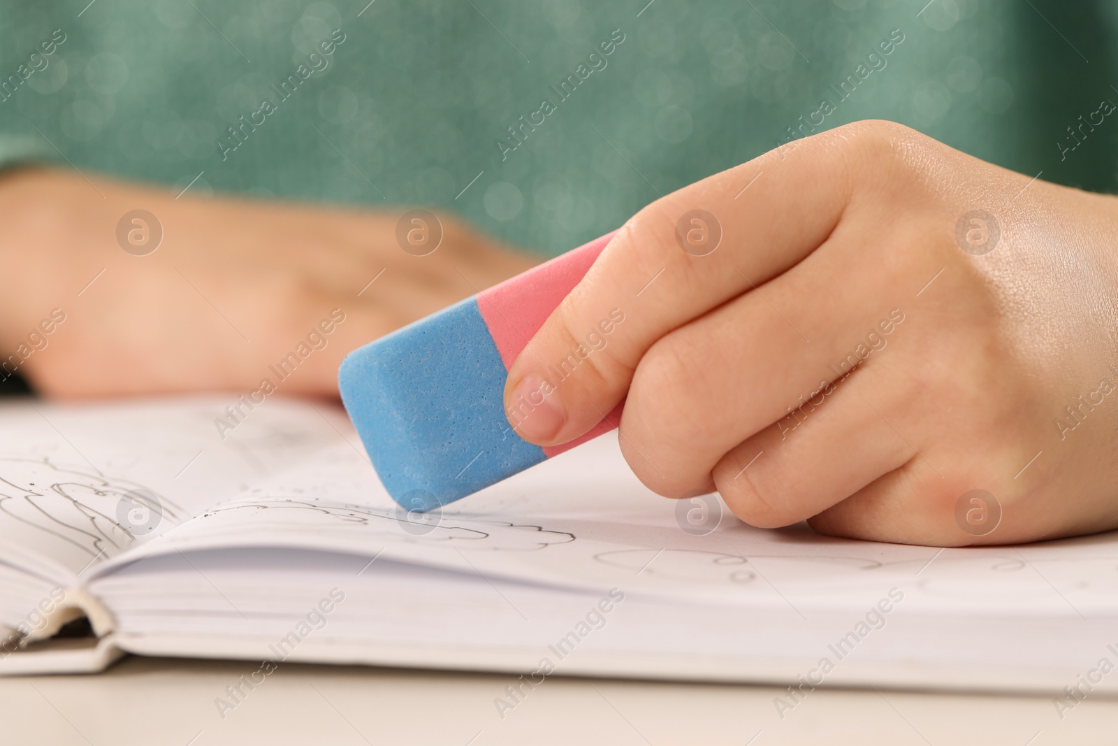 Photo of Girl using eraser at white desk, closeup