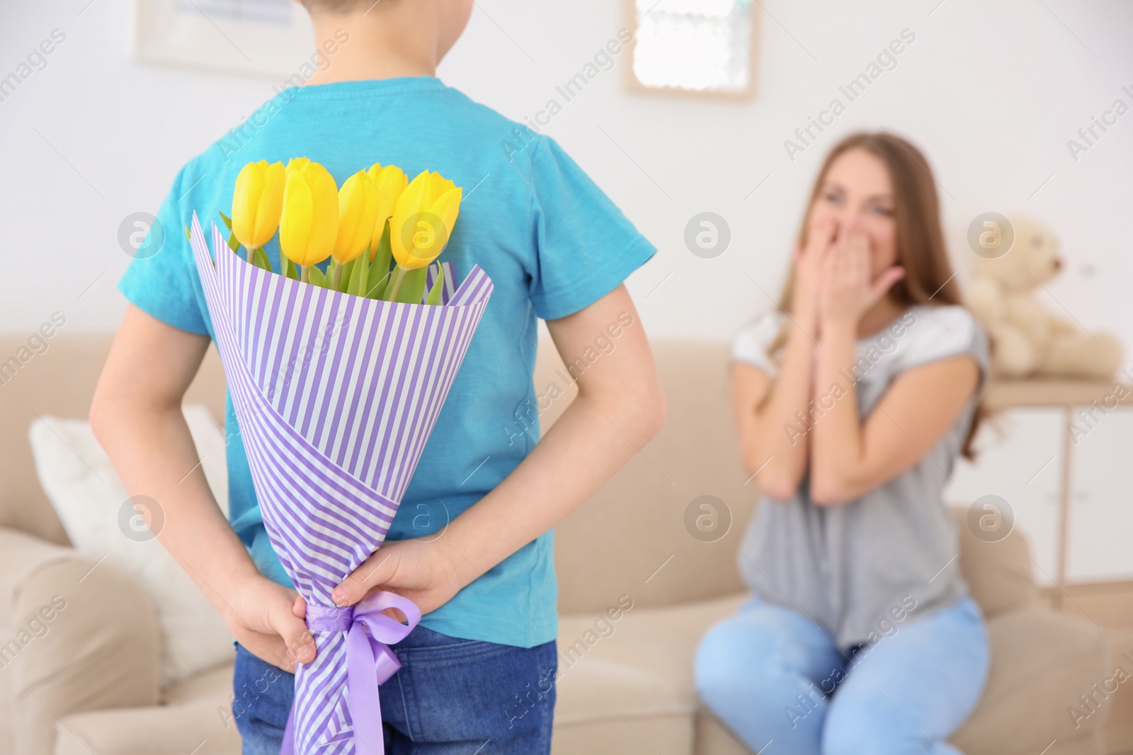 Photo of Little boy hiding tulip bouquet for mother behind his back at home