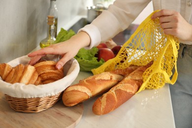 Photo of Woman taking baguettes out from string bag at countertop, closeup