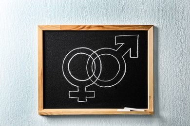 Small blackboard with drawn gender symbols on white wall. Sex education