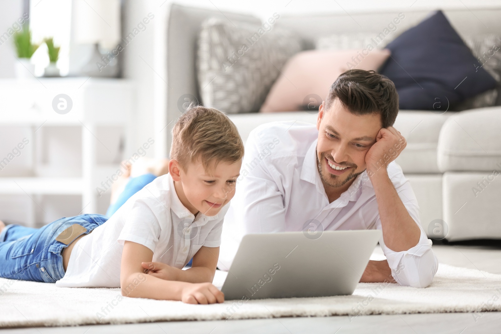 Photo of Little boy and his dad using laptop at home