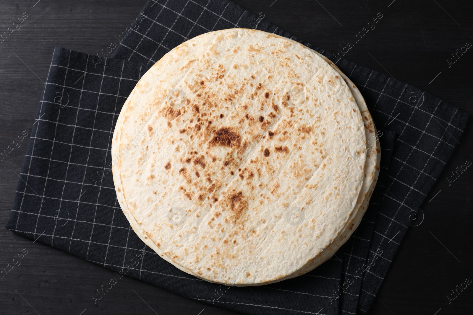 Photo of Many tasty homemade tortillas on black wooden table, top view