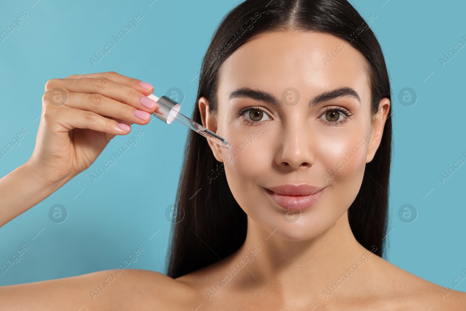 Photo of Beautiful young woman applying serum onto her face on light blue background