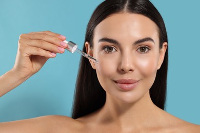 Photo of Beautiful young woman applying serum onto her face on light blue background