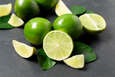 Fresh ripe limes and leaves on black table, closeup