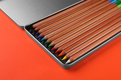 Photo of Box with many colorful pastel pencils on orange background, closeup. Drawing supplies