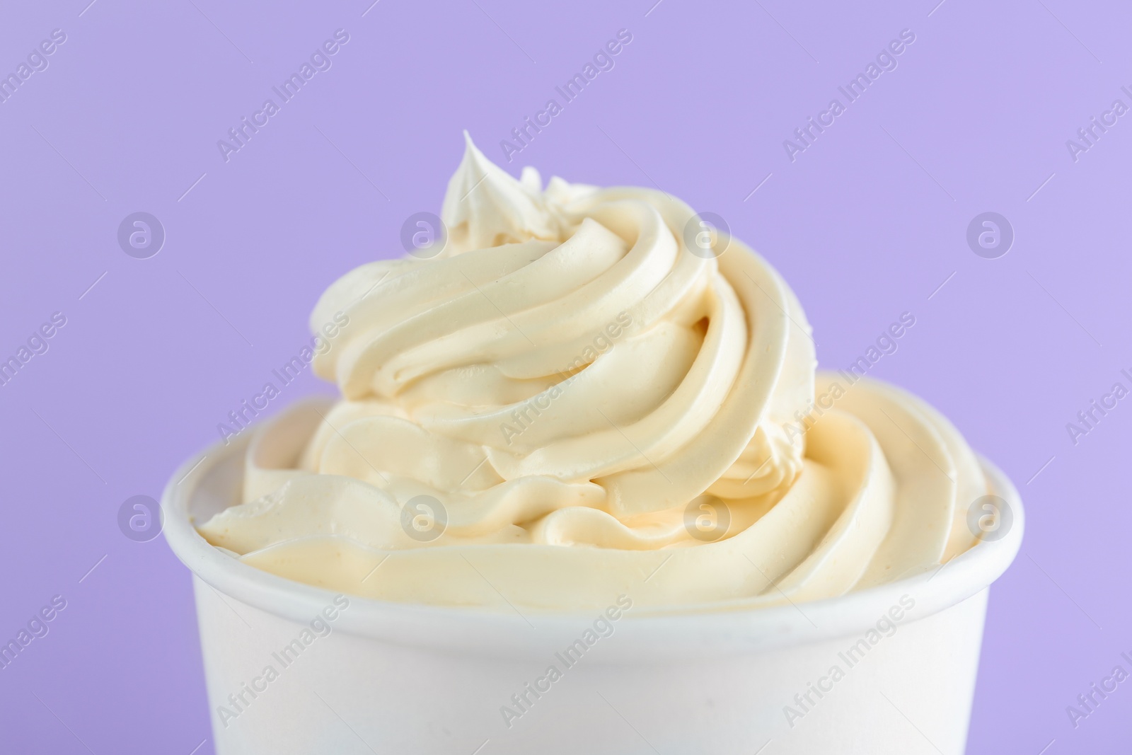 Photo of Cup with tasty frozen yogurt on violet background, closeup