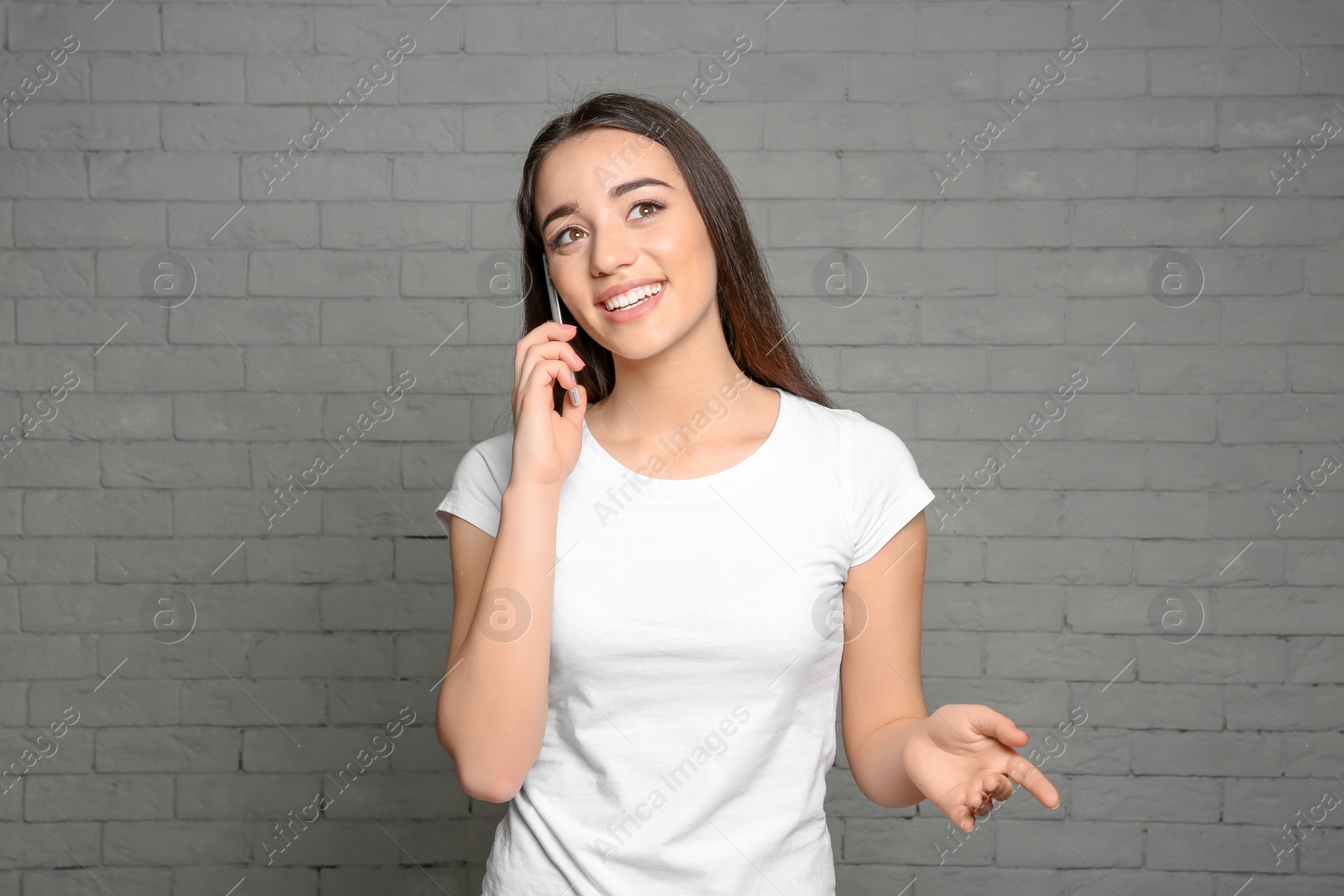 Photo of Attractive young woman talking on mobile phone against brick wall background