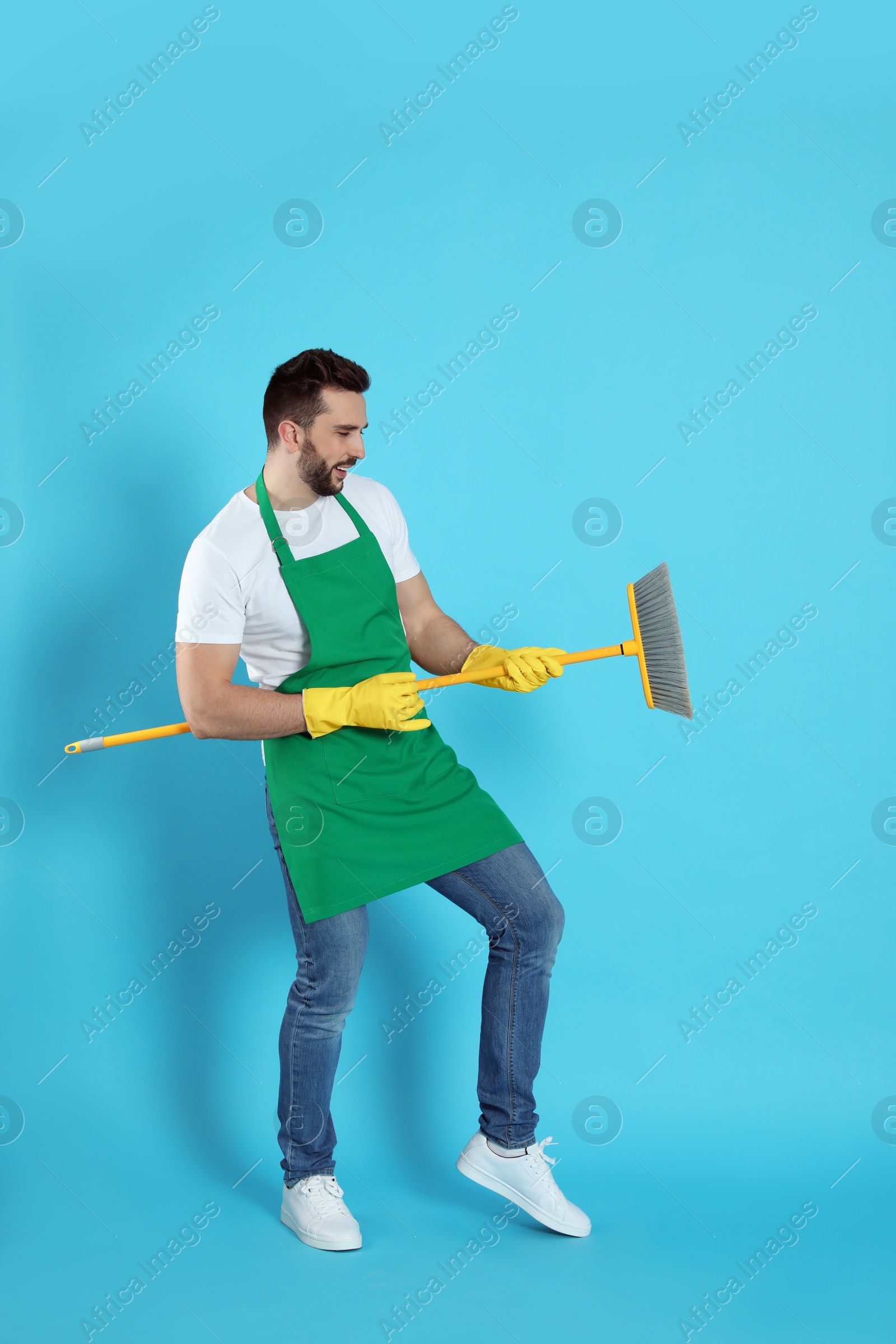 Photo of Man with yellow broom having fun on light blue background