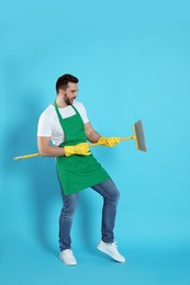 Man with yellow broom having fun on light blue background