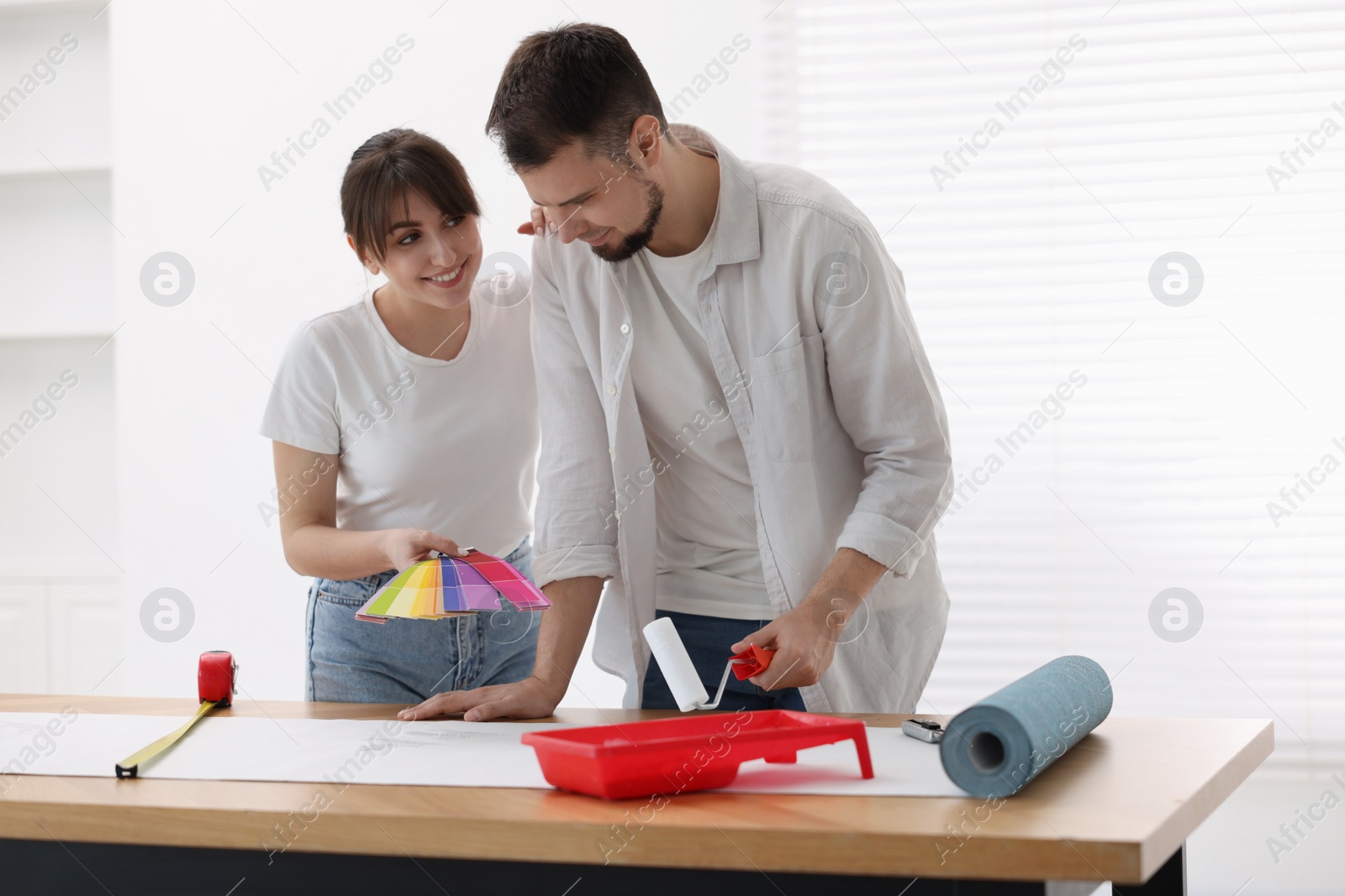 Photo of Woman and man applying glue onto wallpaper sheet at wooden table indoors