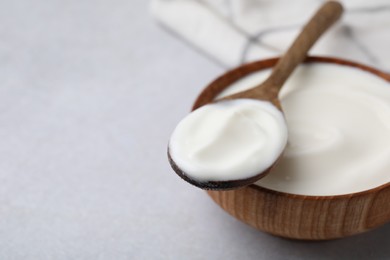 Delicious natural yogurt in bowl and spoon on light grey table, closeup. Space for text