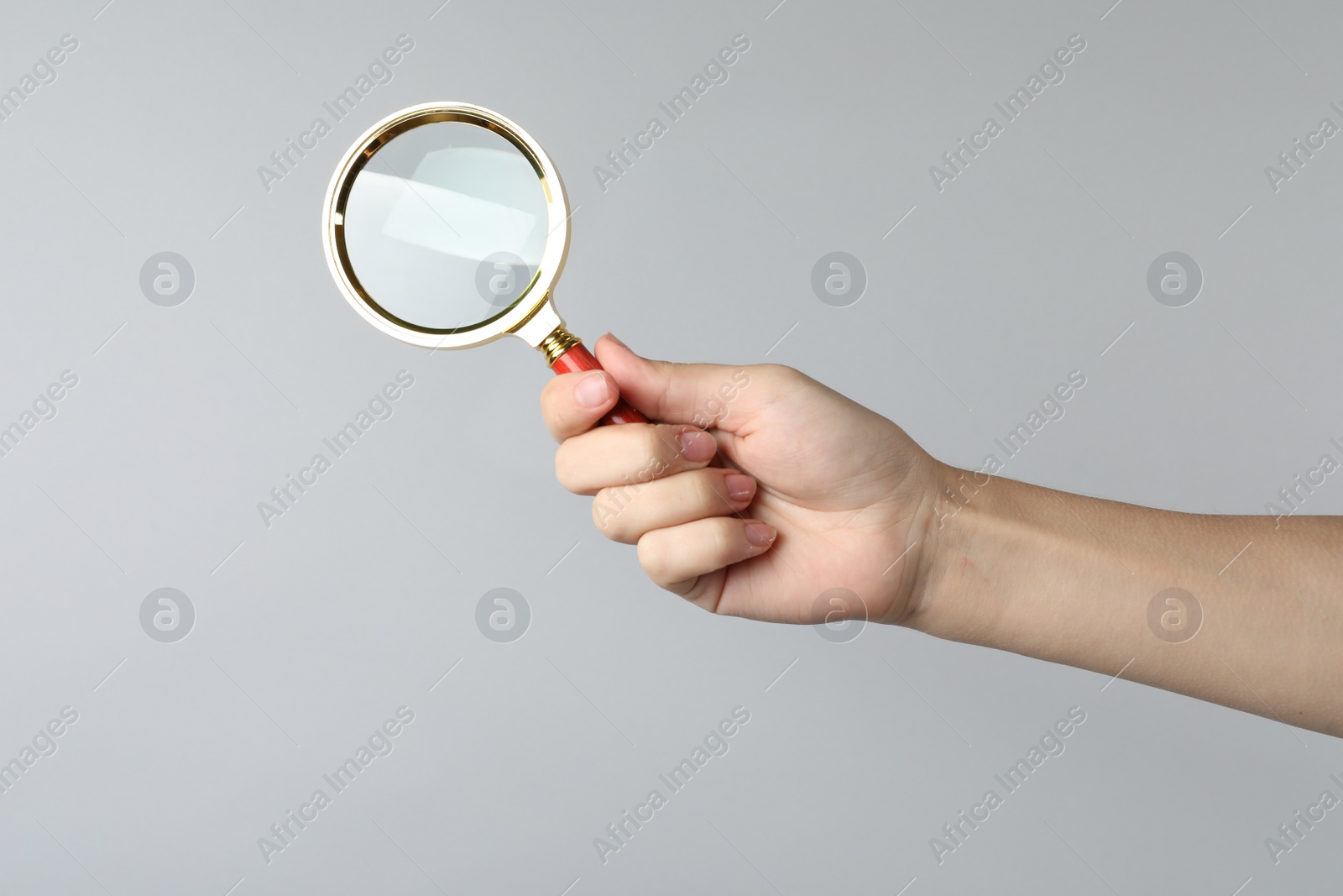 Photo of Woman holding magnifying glass on grey background, closeup. Find keywords concept