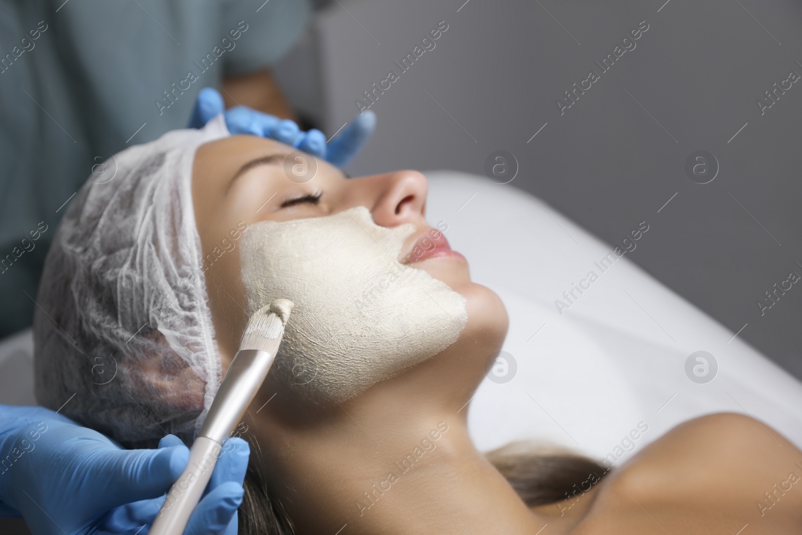 Photo of Cosmetologist applying mask on client's face in spa salon