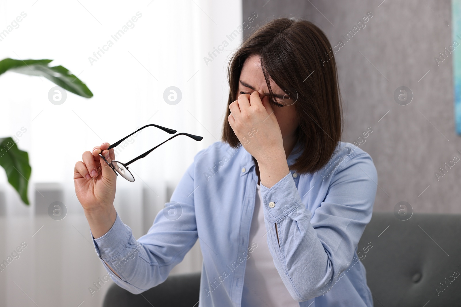 Photo of Overwhelmed woman with glasses sitting on sofa indoors