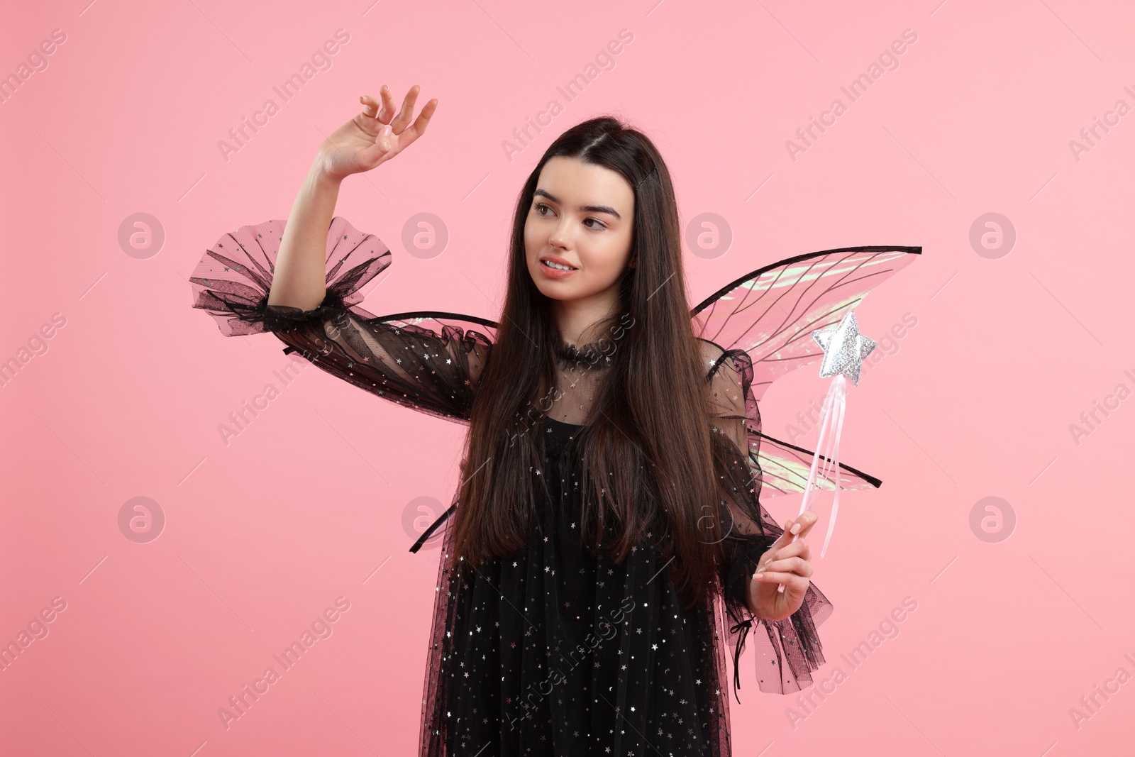 Photo of Beautiful girl in fairy costume with wings and magic wand on pink background