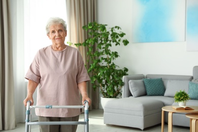 Photo of Elderly woman using walking frame indoors. Space for text
