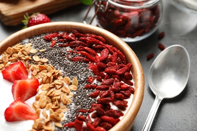 Photo of Smoothie bowl with goji berries and spoon on grey table, closeup