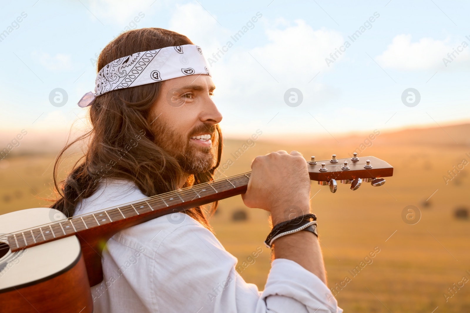 Photo of Portrait of happy hippie man with guitar in field