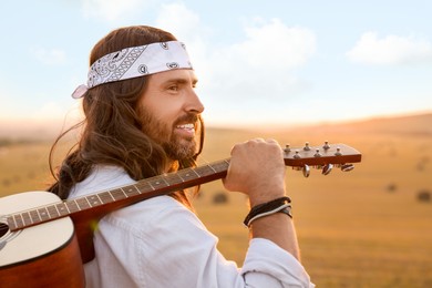 Portrait of happy hippie man with guitar in field