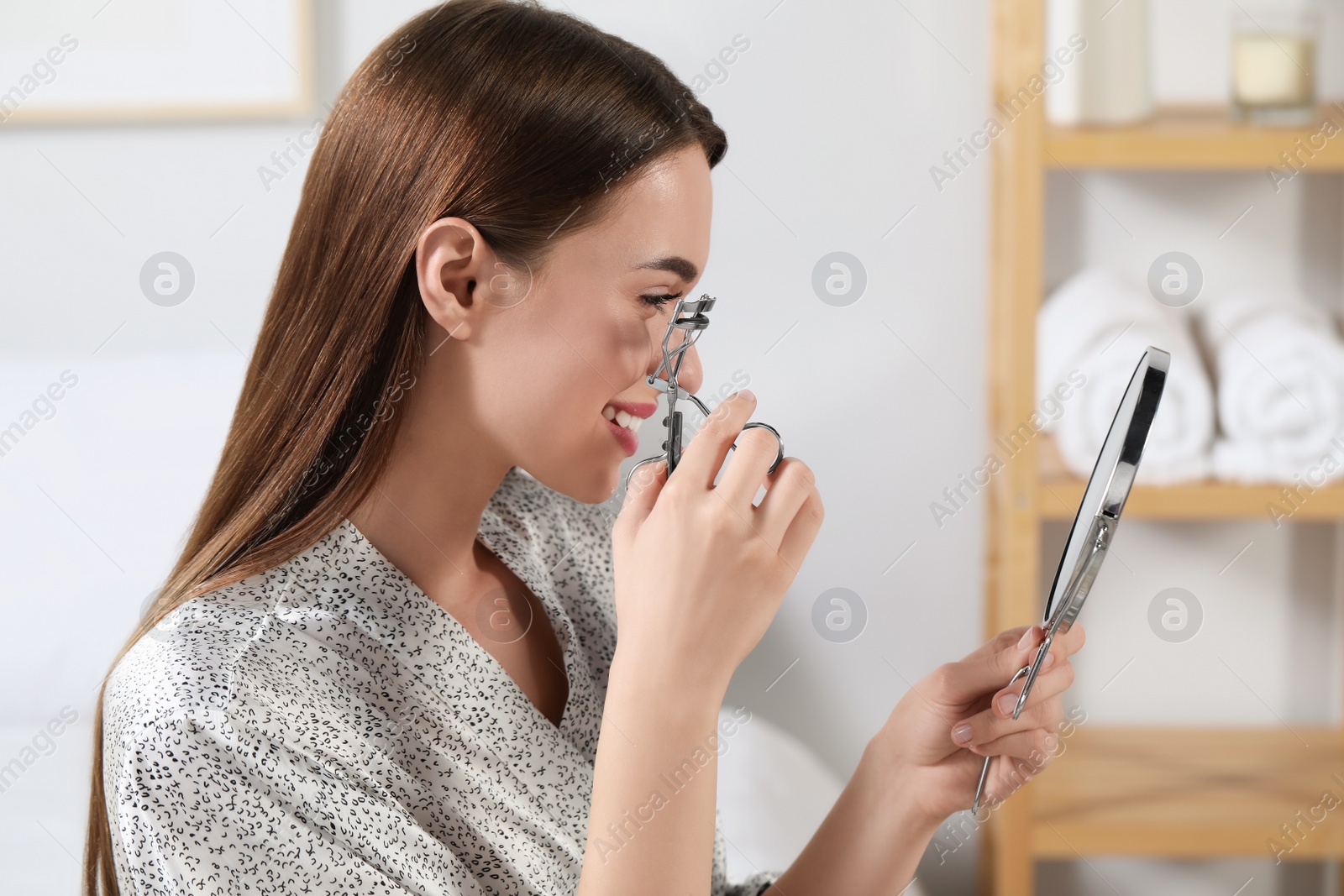 Photo of Woman using eyelash curler near mirror at home