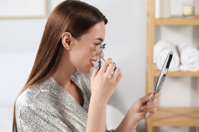 Woman using eyelash curler near mirror at home