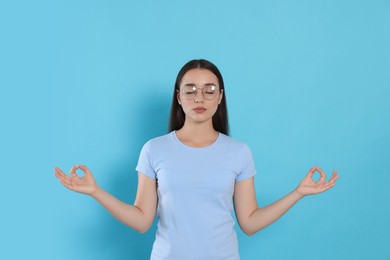 Photo of Find zen. Beautiful young woman meditating on light blue background